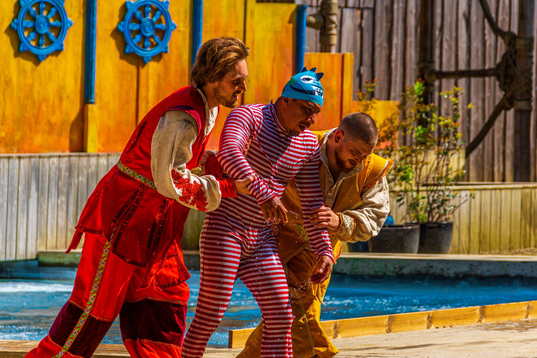 Lakei Pasha wordt met zijn gestreept zwempak door 2 kandidaten begeleid tijdens de Azuria The Next Sultan Stunt & Dive Show.