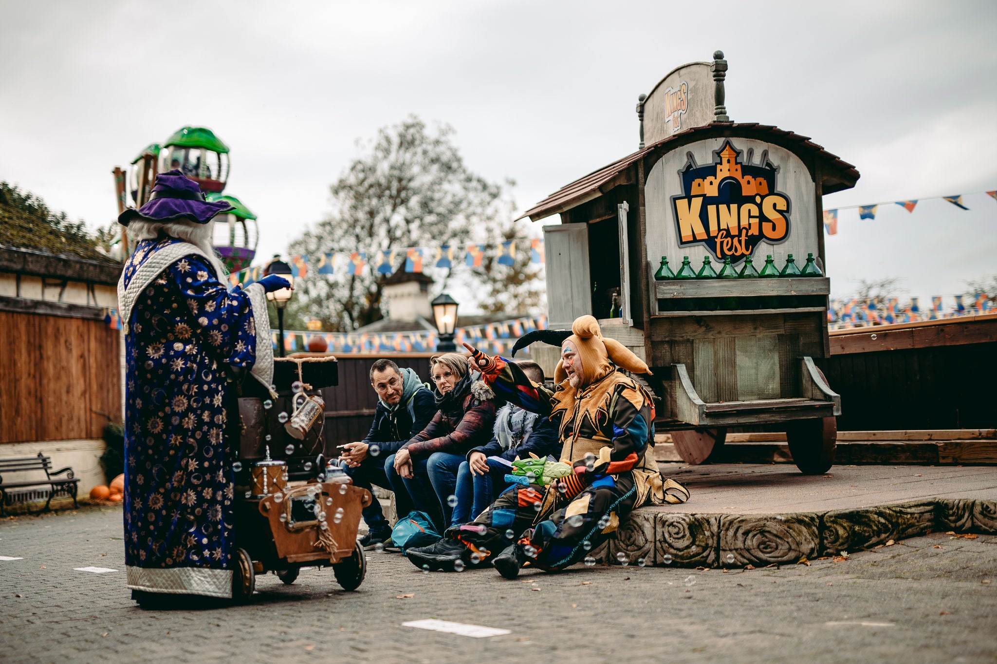 Tovenaar goochelt voor de bezoekers tijdens King’s Fest. Ze zitten samen met een nar voor een woonwagen.