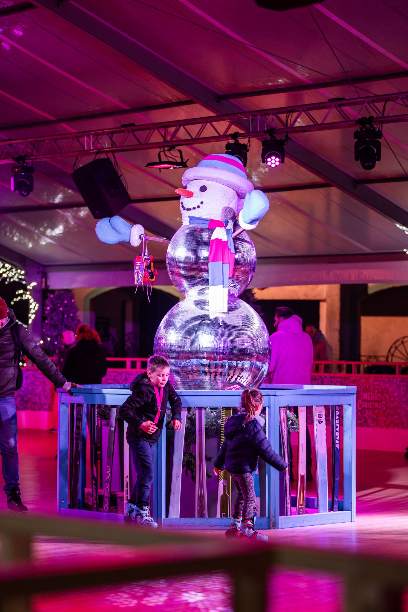 Kinderen rolschaatsen rond een sneeuwman gemaakt van discobollen als kerstdecoratie in Azetec Roller.